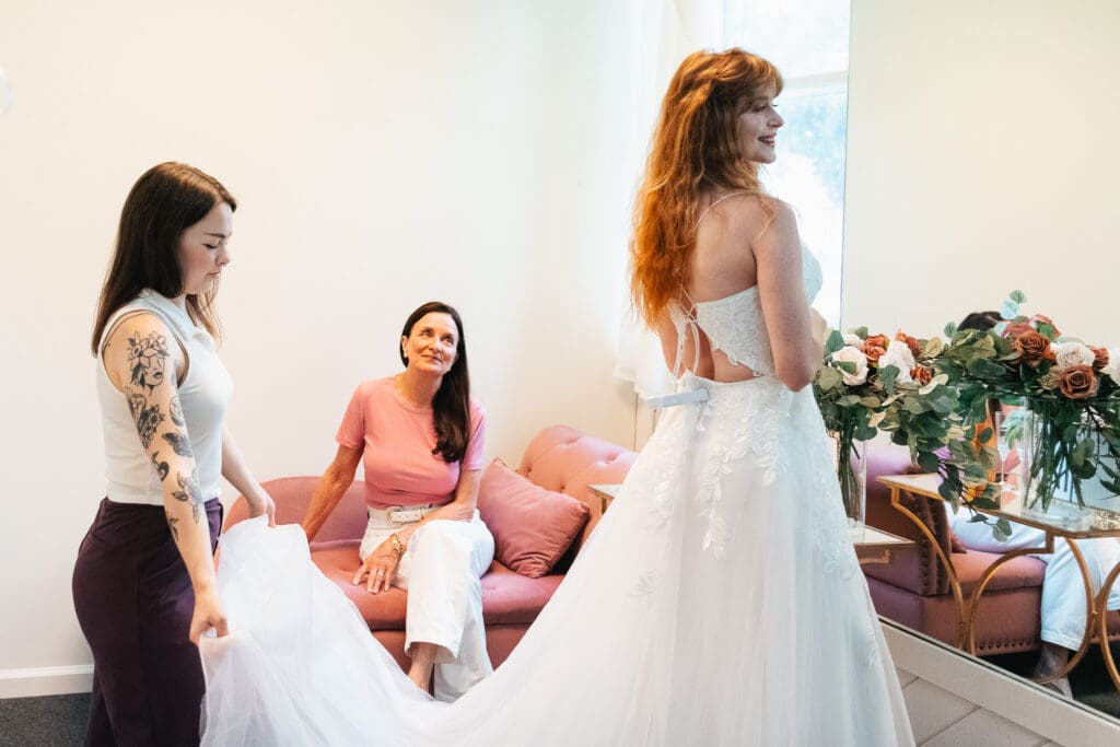 Bride is choosing wedding dress shops in New Jersey and trying a bridal gown with her mom and the a help of a stylist.